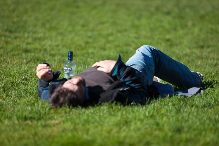 A man lying down for help next to a vodka bottle.