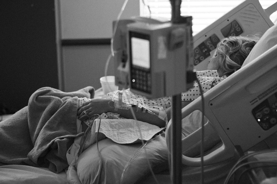 Black-and-white image of a woman lying on a hospital bed with IVs attached to her hand.