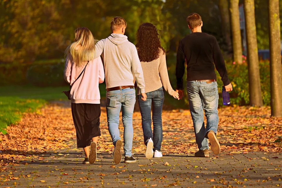 Four friends walking in a park while holding hands.